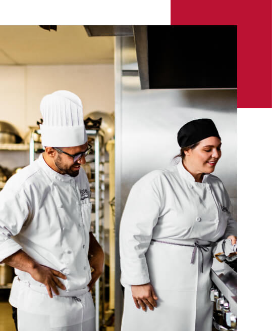 a culinary arts instructor watches a culinary student cook in a commercial kitchen